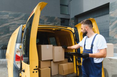 Teslimatçı, sokakta park etmiş sarı bir minibüsün içindeki karton kutuları incelerken envanteri kontrol ediyor.