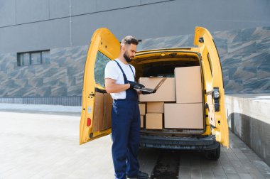 Eldiven takan kurye, karton kutuları kontrol ederken açık teslimat minibüsünün yanında duruyor.