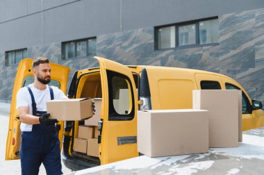 Karton kutuları sarı bir kargo kamyonundan boşaltan kurye nakliye ve lojistik için mal ve paket taşıyor.