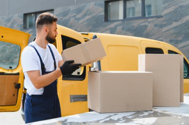 Karton kutuları sarı bir minibüse yükleyen teslimatçı sevkiyat ve dağıtım için hazırlanıyor.