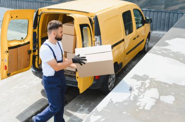 Parlak sarı bir minibüsten paket taşıyan teslimatçı nakliye ve lojistik hizmetlerinin özünü somutlaştırıyor.