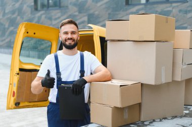 Karton kutular ve sarı teslimat minibüsünün yanında işaret panosu tutan kurye.