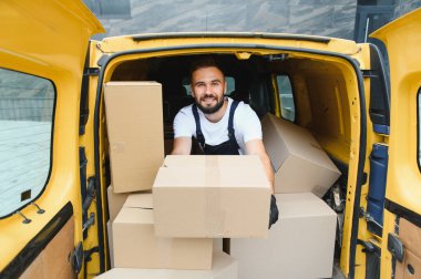 Paketlerle dolu sarı bir minibüsten karton bir kutu getirirken kurye gülümsüyor, alıcıya verimli hizmet sunuyor