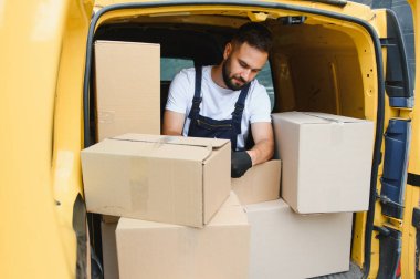 Eldiven takan kurye, sarı bir minibüsün içinde karton kutuları düzenliyor, paketlerin taşınması ve taşınması için hazırlanıyor.