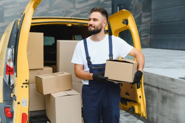 Eldiven takan kurye, elinde bir paket, paketlerle dolu bir teslimat aracının yanında duruyor.