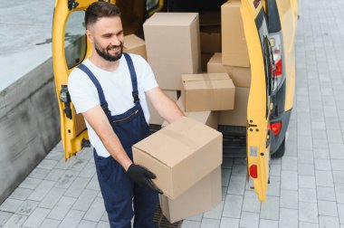 Parlak sarı bir minibüsten paketleri boşaltan gülümseyen teslimatçı verimli lojistik operasyonların bir parçası olarak karton bir kutu taşıyordu.