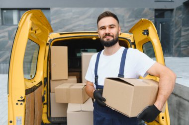 Paketlerle dolu sarı bir minibüsten paketleri indirirken bir paket taşıyan teslimatçı etkili lojistik ve ulaşım hizmeti sunuyor.
