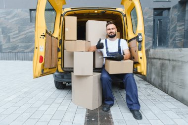 Karton kutularla dolu bir minibüste teslimat listesi tutarken kurye onay veriyor.