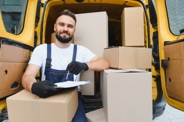 Karton kutularla dolu bir minibüste otururken kurye pano tutuyor ve paketlerin listesini kontrol ediyor