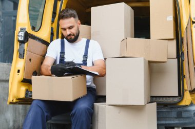 Karton kutularla dolu bir minibüste paket listesini kontrol ederken panoya kurye yazma