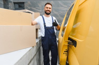 Tulum ve eldiven giyen kurye, sarı bir teslimat minibüsü ve karton kutuların yanına başparmak işareti veriyor. Nakliye ve teslimat için hazır.