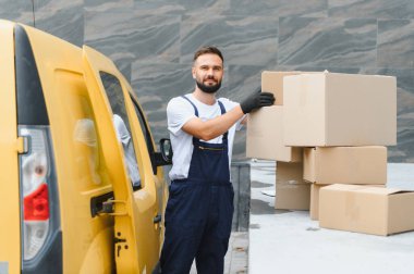 Eldiven giyen kurye, şehir sokağındaki parlak sarı bir minibüsten karton kutuları indiriyor ve paketleri etkili bir şekilde taşıyor.