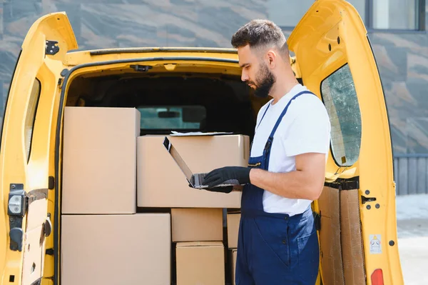 Kurye, karton kutularla dolu sarı minibüsün yanındaki dizüstü bilgisayarda teslimat bilgilerini kontrol ediyor, sevkiyat ve lojistik işlerini yönetiyor.