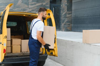 Karton kutuları parlak sarı bir minibüsten boşaltan teslimatçı, malları doğrudan müşterilerin kapısına taşıyor.