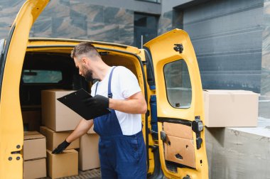 Eldiven takan kurye, sarı bir minibüste pano tutarken karton kutuları kontrol ediyor.