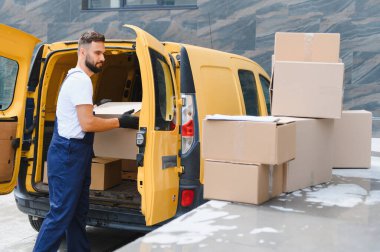 Paketleri bir teslimat aracına yükleyen kurye, şehir sokaklarında verimli sevkiyat ve mal dağıtımına hazırlanıyor.
