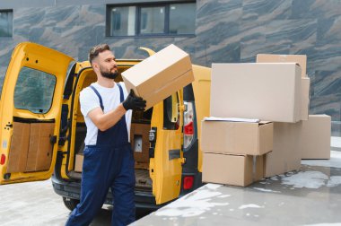 Kurye, karton kutuları sarı bir kargo kamyonundan boşaltıyor. Malları verimli ve güvenilir bir şekilde taşıyor.