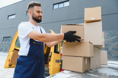 Eldiven giyen kurye, deponun yakınındaki bir arabanın çatısında karton kutuları istifleyerek verimli teslimata hazırlanıyor.