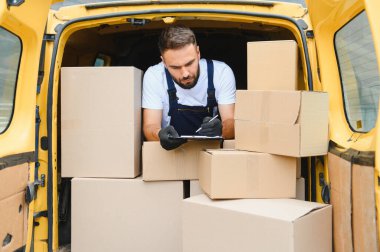 Kurye teslimat minibüsündeki paketleri kontrol ederken panoya notlar yazıyor, doğru teslimat ve müşteri memnuniyeti sağlanıyor