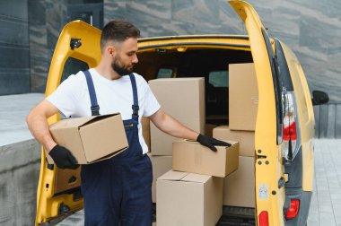 Eldiven takan kurye, karton kutuları binanın yakınına park etmiş sarı bir minibüse yüklüyor.