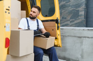 Karton kutular, teslimat ve nakliye hizmeti konseptiyle dolu bir minibüste paketler listesini kontrol ederken kurye panosuna yazı yazma