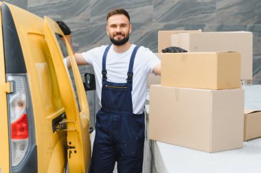 Tulum giyen kurye, parlak sarı bir teslimat kamyonetinden karton kutuları boşaltıyor, ulaşım ve lojistik için paketleri etkili bir şekilde yönetiyor.