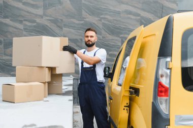 Eldiven giyen kurye, parlak sarı bir teslimat kamyonetinin yanından karton bir kutu alıyor. Verimli lojistik ve ulaşım sektöründe çalışıyor.