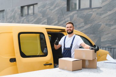 Kurye, parlak sarı bir teslimat kamyonetinin yanında karton kutular tutarken olumlu ve güvenilirlik yayıyor.