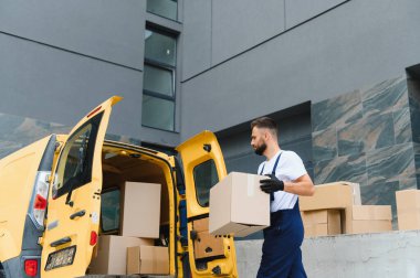 Kurye, parlak sarı bir teslimat kamyonundan karton kutuları indiriyor. Malları doğrudan müşterilerin kapısına taşıyor.