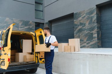 Kurye, karton kutuları sarı bir kargo kamyonundan boşaltıyor, verimli ve güvenilir nakliye için mal ve paket taşıyor.