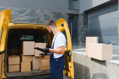 Koruyucu maske takan ve eldiven takan kurye, karton kutuları karton bir minibüsle kontrol ediyor.