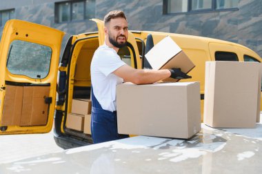 Kurye, açık teslimat kamyonetinin yanında karton kutular taşırken yüzünü buruşturan eldivenler giyerek hayal kırıklığını ve zorluğu ifade ediyor.