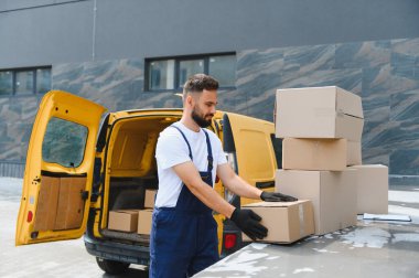 Eldiven takan kurye, sarı bir minibüsten karton kutuları indiriyor ve verimli dağıtım için paketler düzenliyor.