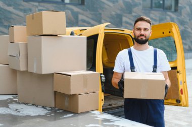 Paket teslimatçısı, sarı bir minibüsün yanında dururken, daha fazla paket teslimatı için hazır bekliyor.