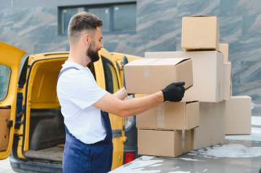 Teslimatçı, karton kutuları sarı minibüsünün üstüne yerleştiriyor, nakliye ve taşıma için hazırlanıyor.