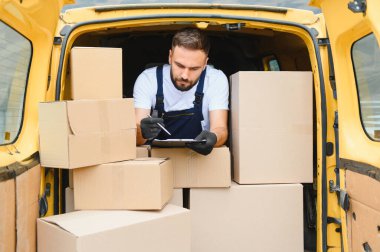 Karton kutularla dolu bir minibüsün içindeki paketleri kontrol ederken panoya eldiven yazan bir kurye.