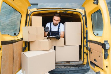 Dijital tablet kullanarak karton kutuları doğrulayan kurye açık teslimat minibüsünde otururken, doğru nakliye ve lojistik