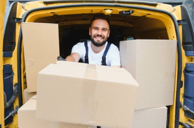 Verimli nakliye için çeşitli paketlerle dolu sarı bir minibüsten bir müşteriye karton kutu teslim eden gülümseyen bir teslimatçı.