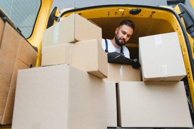 Karton kutuları bir teslimat minibüsünde incelerken bir panoya kurye notları yazarak verimli bir lojistik ve sipariş doğruluğu sağlar.