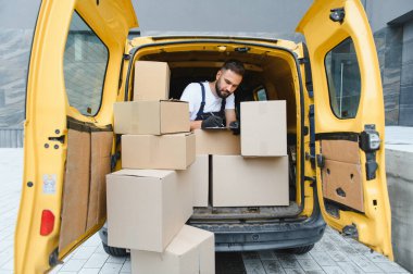 Ticari bir aracın içindeki karton kutuları kontrol ederken bir panoya kurye yazması, verimli hizmet için teslimatları yönetmek