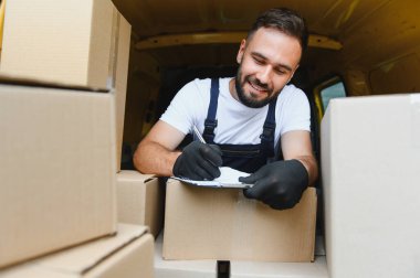 Gülümseyen kurye, karton kutularla dolu minibüsünün içindeki panodaki paket listesini kontrol ediyor.