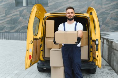 Eldiven takan kurye, karton kutularla dolu sarı minibüsünün yanında bir paket tutuyor.