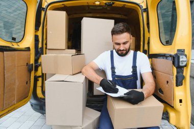 Karton kutularla dolu bir minibüste kargo için paket yönetirken kurye panoya notlar yazıyor.