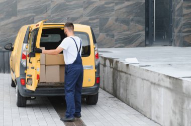 Eldiven giyen kurye, parlak sarı bir teslimat kamyonetinden karton kutuları topluyor. Nakliye için paketleri etkili bir şekilde taşıyor.