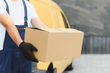 Siyah eldivenli bir teslimatçı, sarı bir kargo aracının yanında karton bir kutu tutuyor, hızlı ve güvenilir bir nakliye hizmeti veriyor.