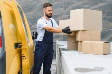 Eldiven giyen kurye, karton kutuları sarı bir kargo kamyonundan indiriyor, paketlerin taşınması ve taşınması için hazırlanıyor.