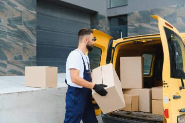 Parlak sarı bir teslimat kamyonetinden bir paket kutusunu müşterinin evine taşıyan kurye.