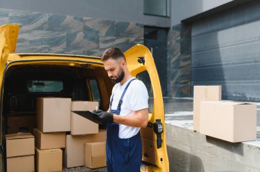 Panoya karton kutularla dolu bir minibüsün yanında kargo ve lojistiği yöneten bir kurye.