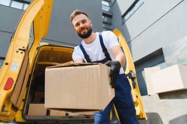 Parlak sarı bir minibüsün arkasından karton bir kutu teslim eden teslimatçı, şehir ortamında güvenilir bir hizmet sağlıyor.