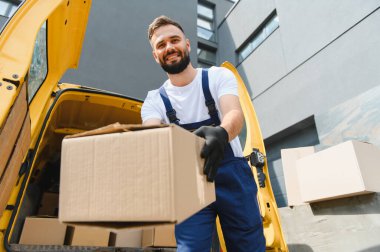 Gülümseyen teslimatçı elinde karton bir kutuyla açık bir teslimat aracının yanında duruyor. Müşterilere verimli hizmet sunmaya hazır.